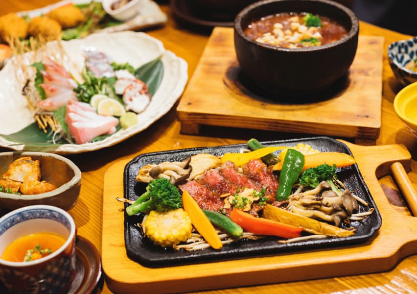 写真：鉄板皿に乗った数種類の焼き屋紙とお肉、そのほかお刺身などの料理