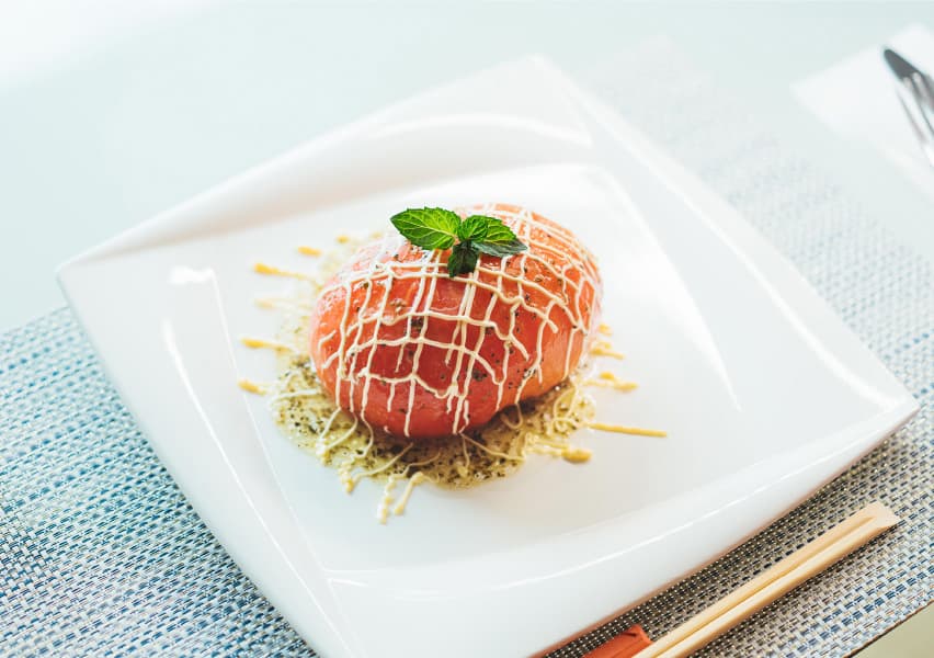 写真；白い皿に盛り付けられた、赤い楕円形の食材に白のソースがかかっている