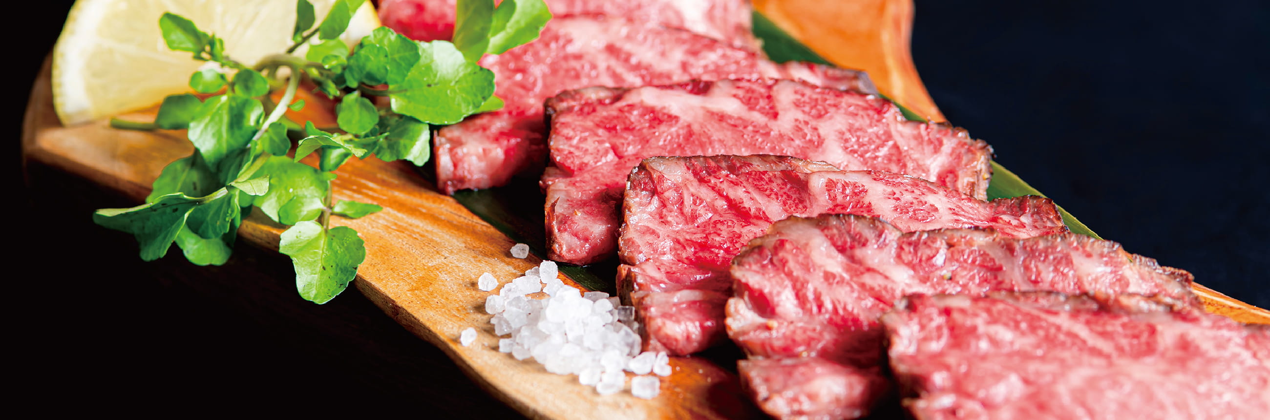写真：木のカッティングボード上に薄く切られたローストビーフが並べられて、周りに岩塩、クレソン、薄く切ったレモンの輪切りが添えられている