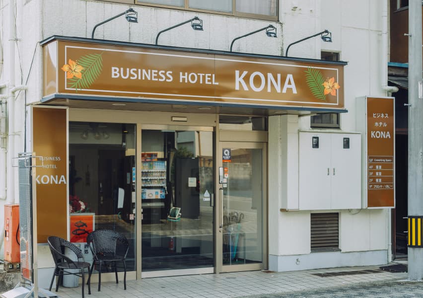 写真：茶色の看板に白字でホテル名が書かれていて、オレンジの花と緑の葉っぱが両脇に描かれている